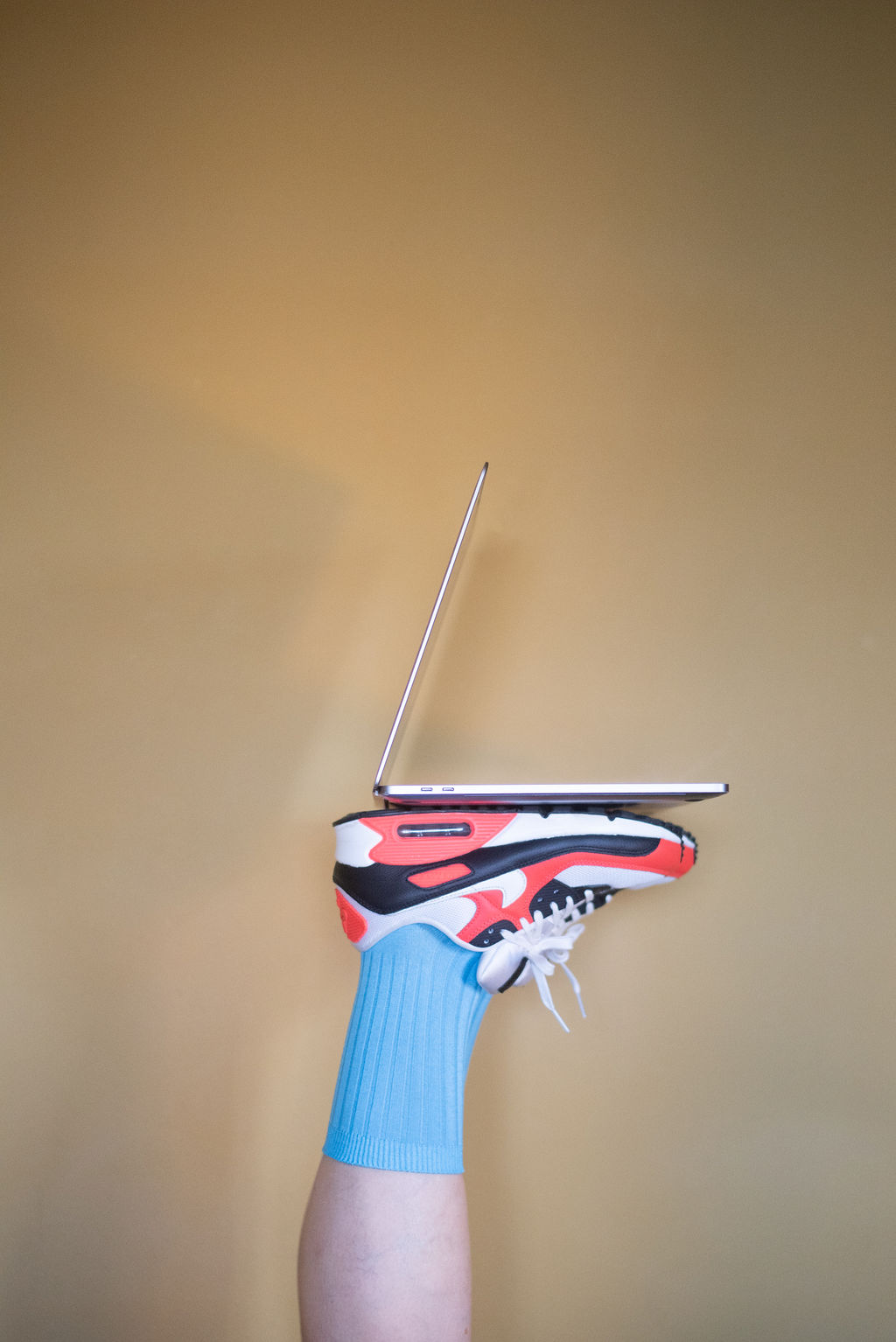 A laptop balanced on colorful sneakers against a warm wall